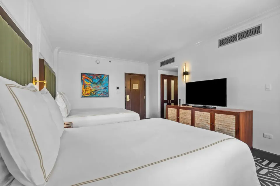 Heritage Queen Room with two queen beds, TV console, entry door, and wall art at Condado Vanderbilt Hotel.