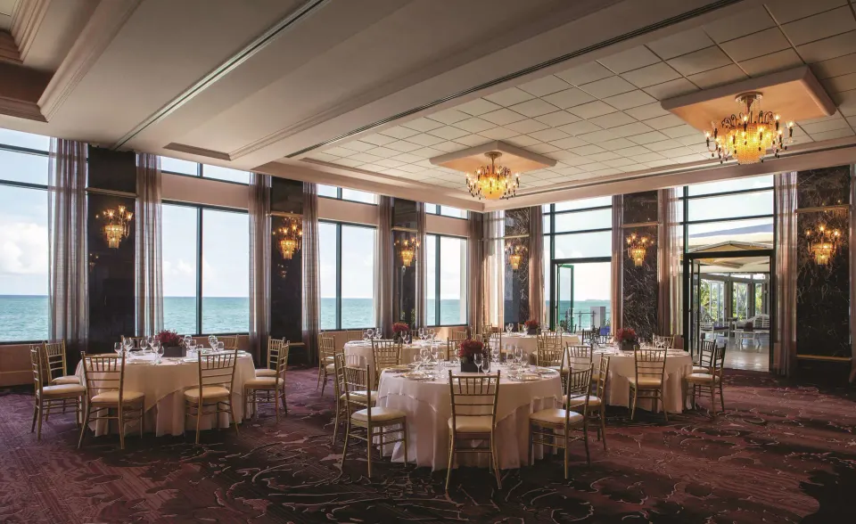 Oceanfront event room with round tables and gold chairs at Condado Vanderbilt Hotel.