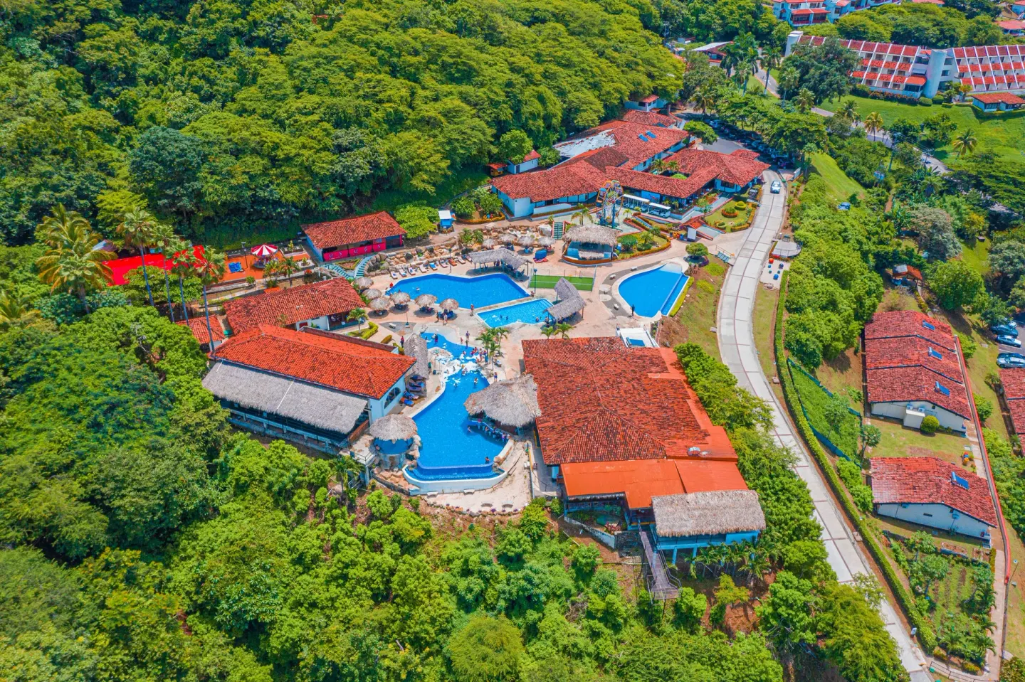 Aerial view of pool areas, red roofs, roads, and trees at Condovac la Costa.