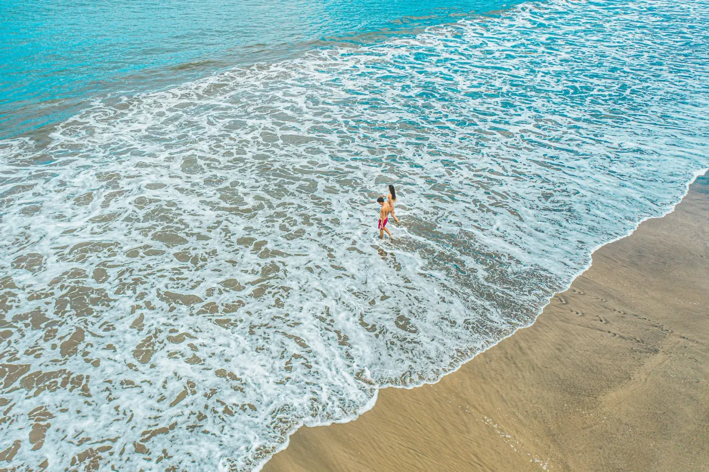 A person wades through foamy surf on the beach at Condovac la Costa.