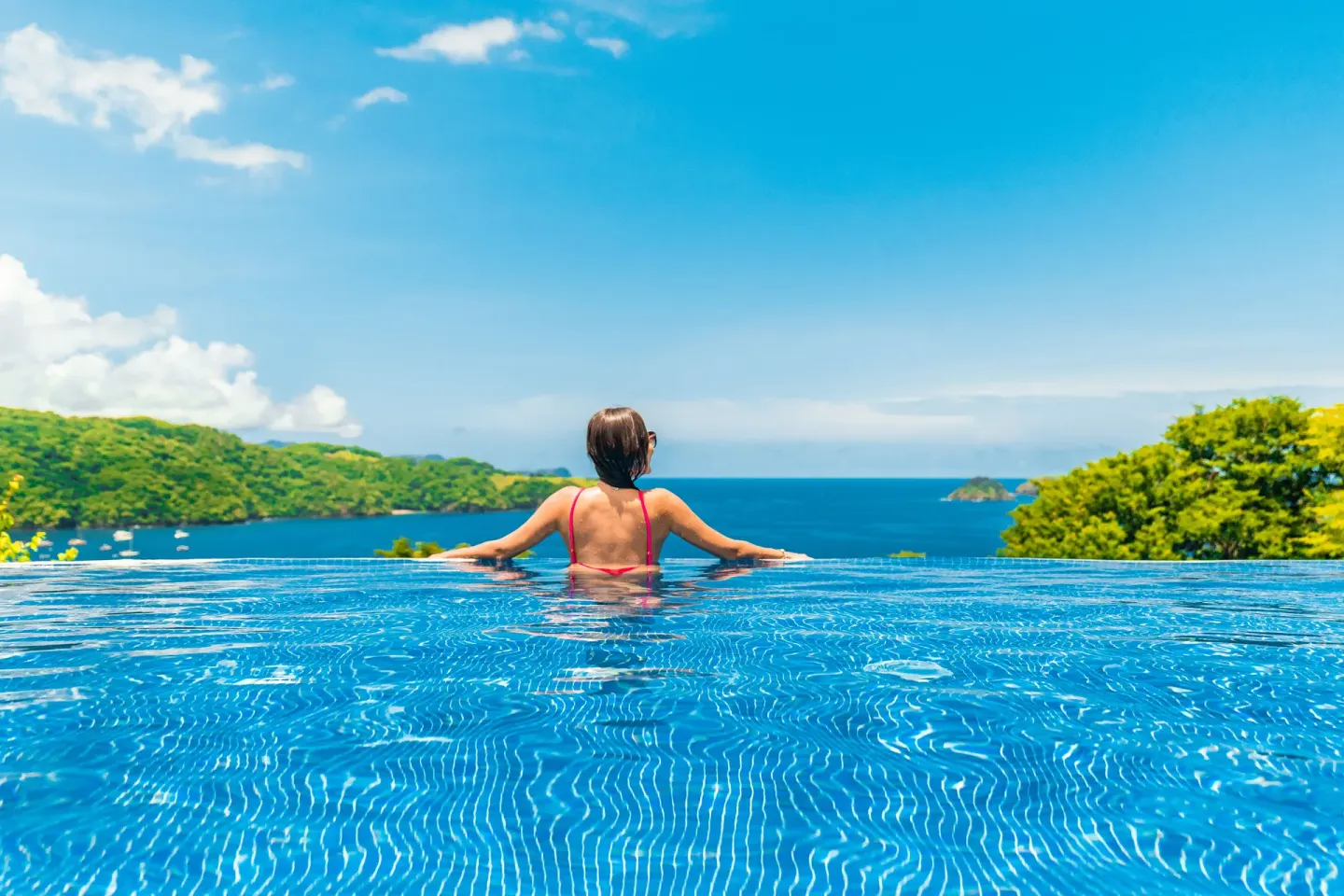 Guest leaning on the infinity pool edge overlooking the bay at Condovac la Costa.