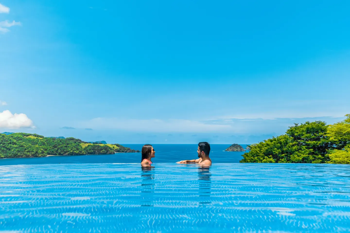 Couple in the infinity pool facing the ocean and islands at Condovac la Costa.