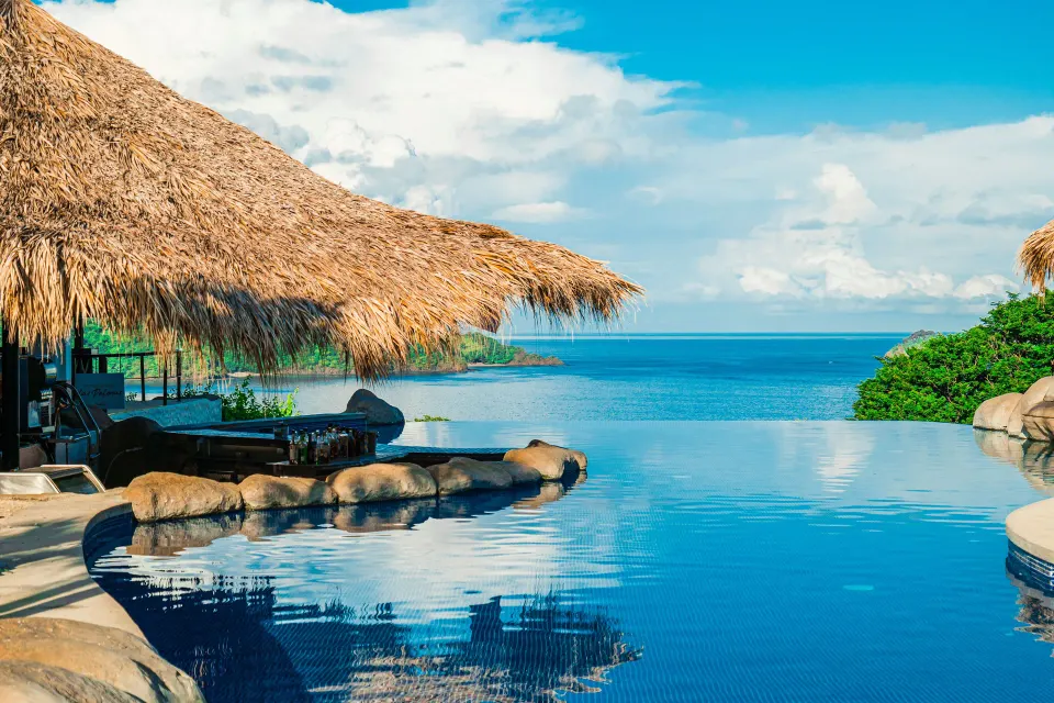 Infinity pool with thatched roof and ocean view at Condovac la Costa.