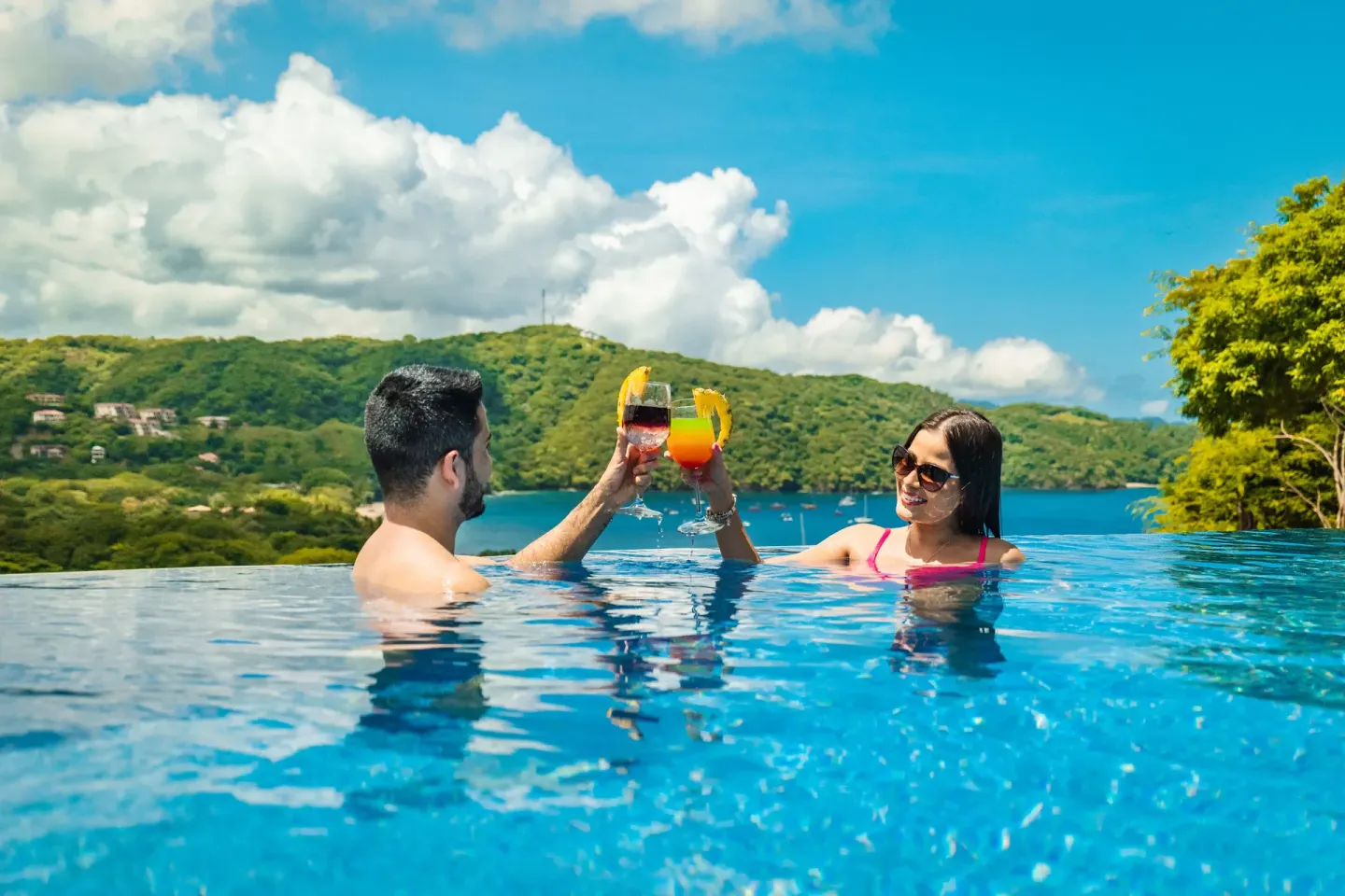 Couple toasting drinks in the infinity pool with bay view at Condovac la Costa.