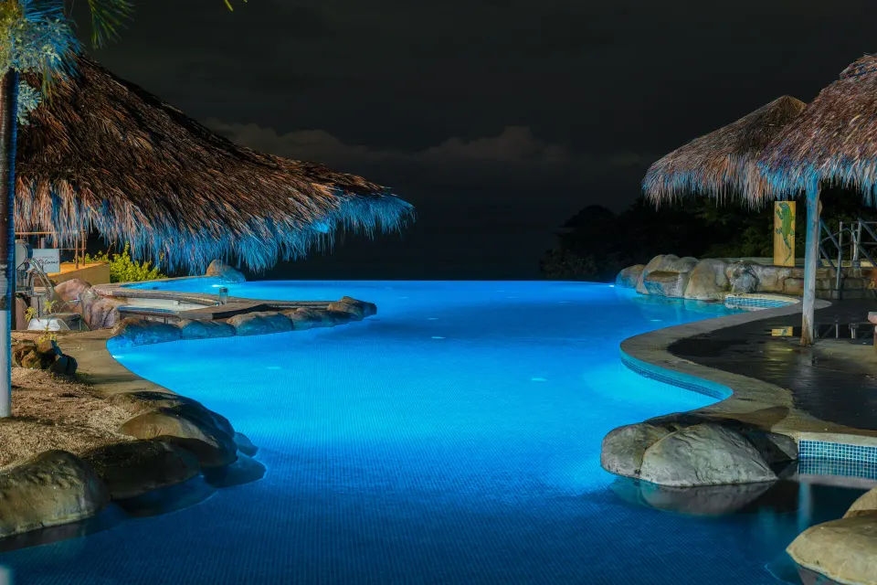 Illuminated resort pool at night with palapa roofs at Condovac la Costa.