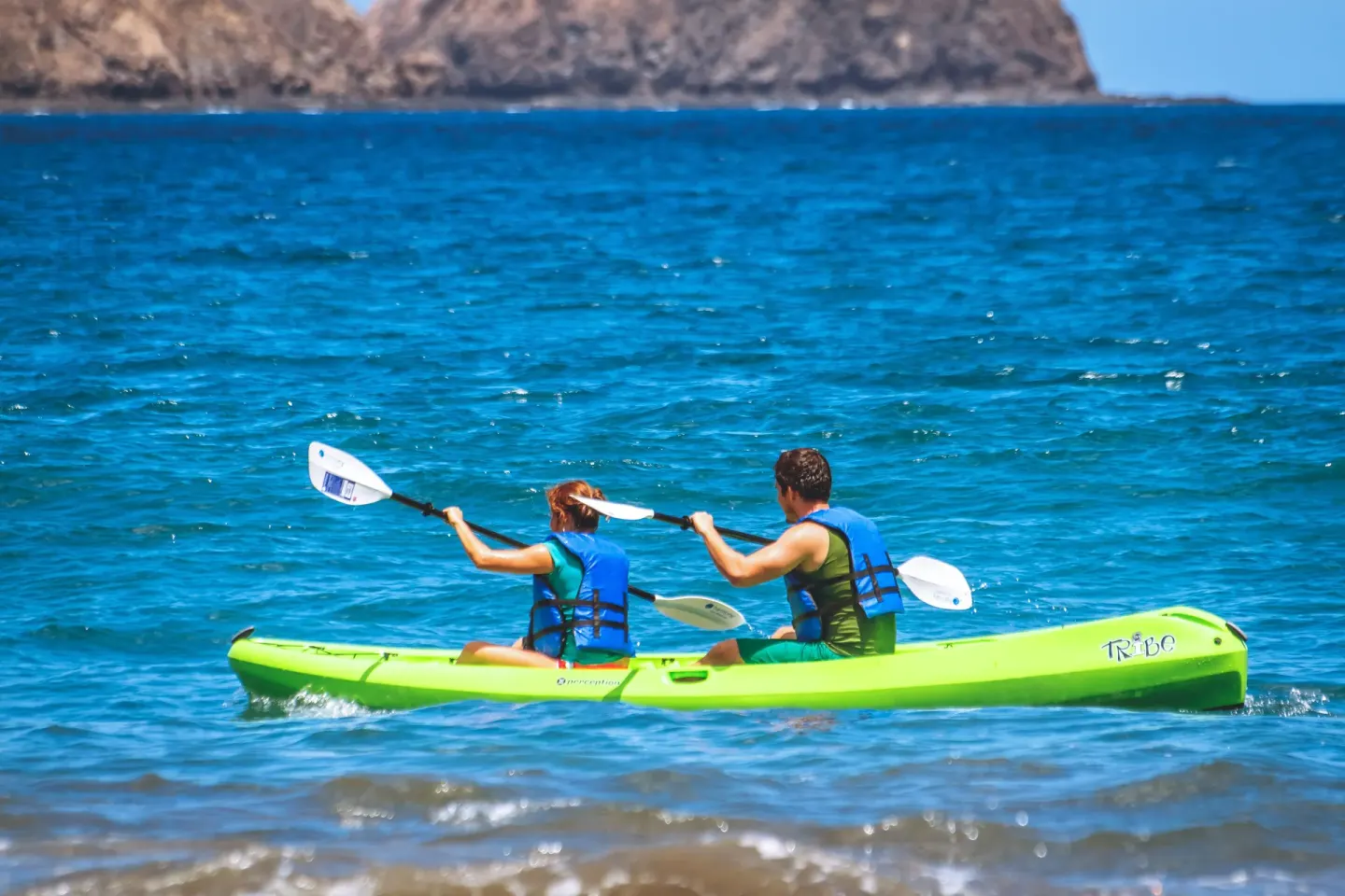 Two people kayak on bright blue ocean water near Condovac la Costa.