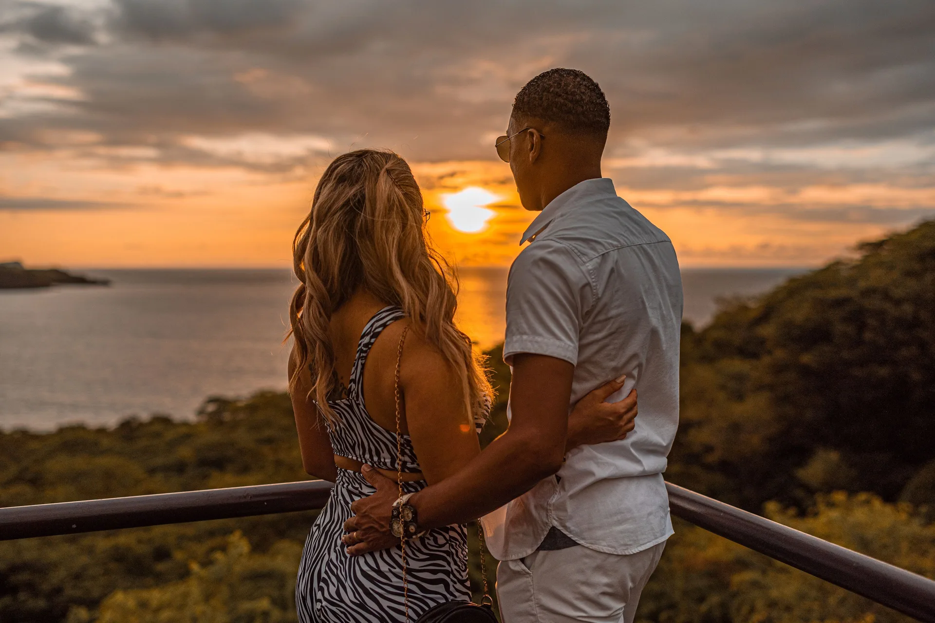 Couple watching an orange ocean sunset from a railing at Condovac la Costa.
