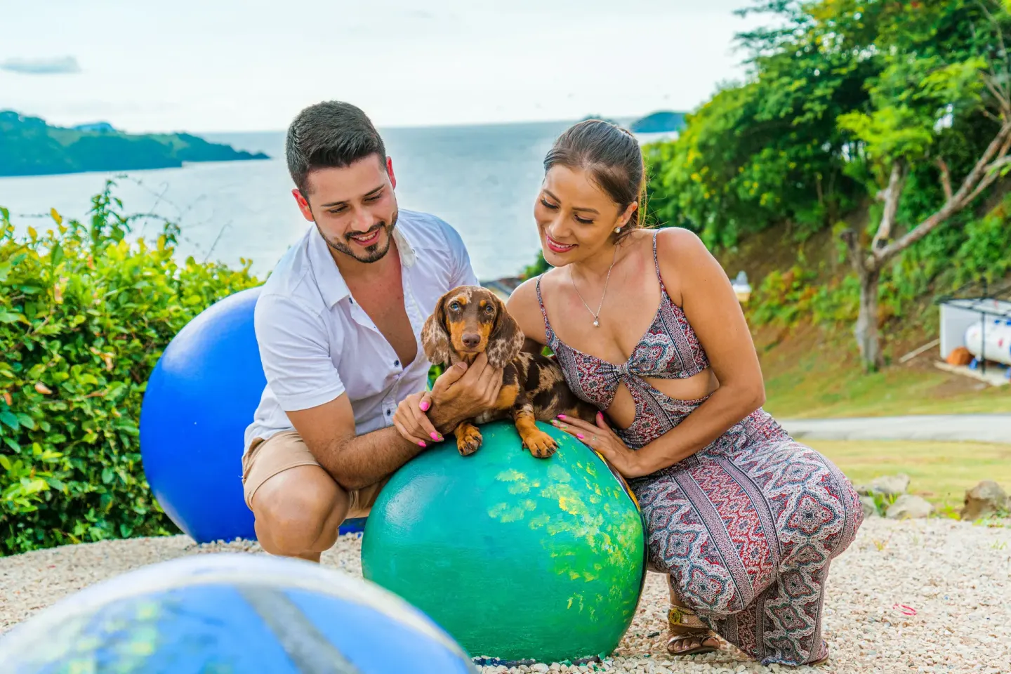 A couple poses with a small dog by colorful spheres and ocean views at Condovac la Costa.