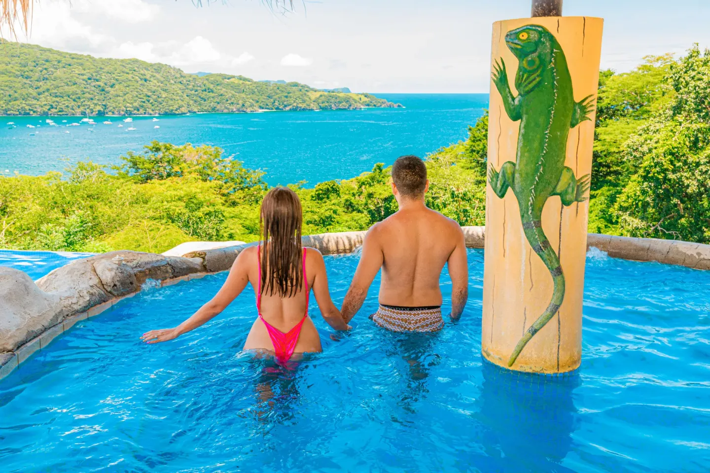 Couple in a pool beside a painted iguana column at Condovac la Costa.