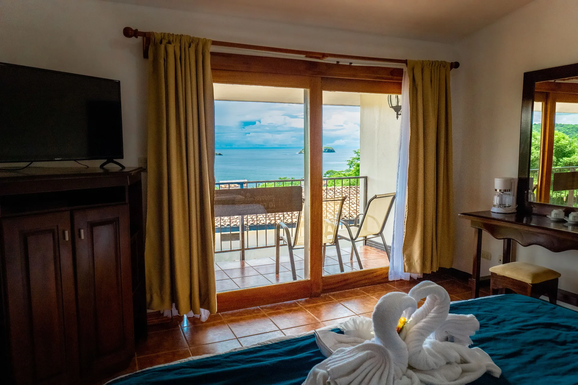 Romantic Studio Suite at Condovac la Costa with bed, balcony seating, TV, and ocean view.