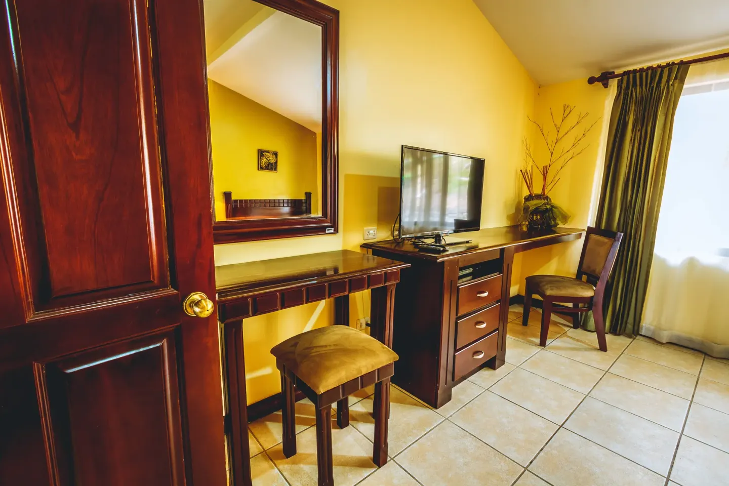 Standard Villa room corner with vanity desk, TV, chair, and mirror at Condovac la Costa.