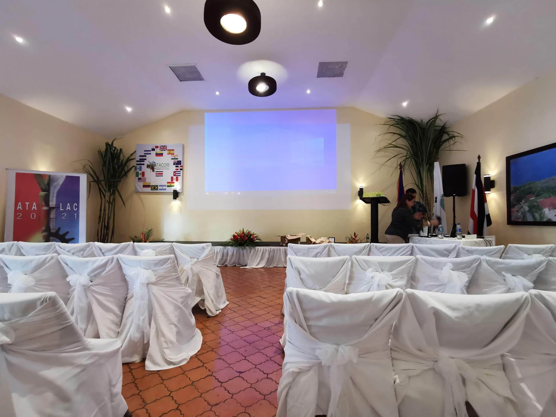 Conference room with white chair covers and a projection screen at Condovac la Costa.