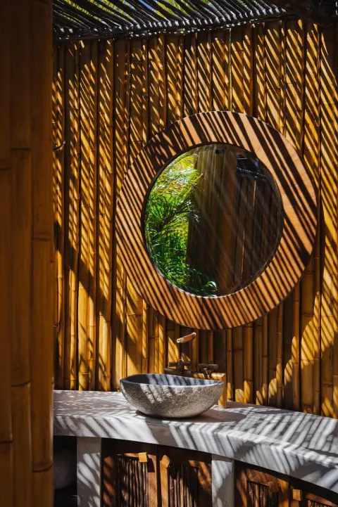 Outdoor stone sink and round mirror in a bamboo-walled space at Conrad Punta de Mita.