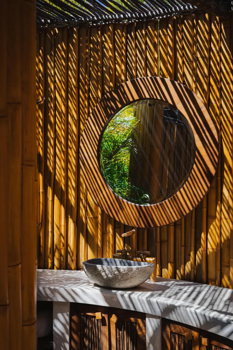 Outdoor stone sink and round mirror in a bamboo-walled space at Conrad Punta de Mita.