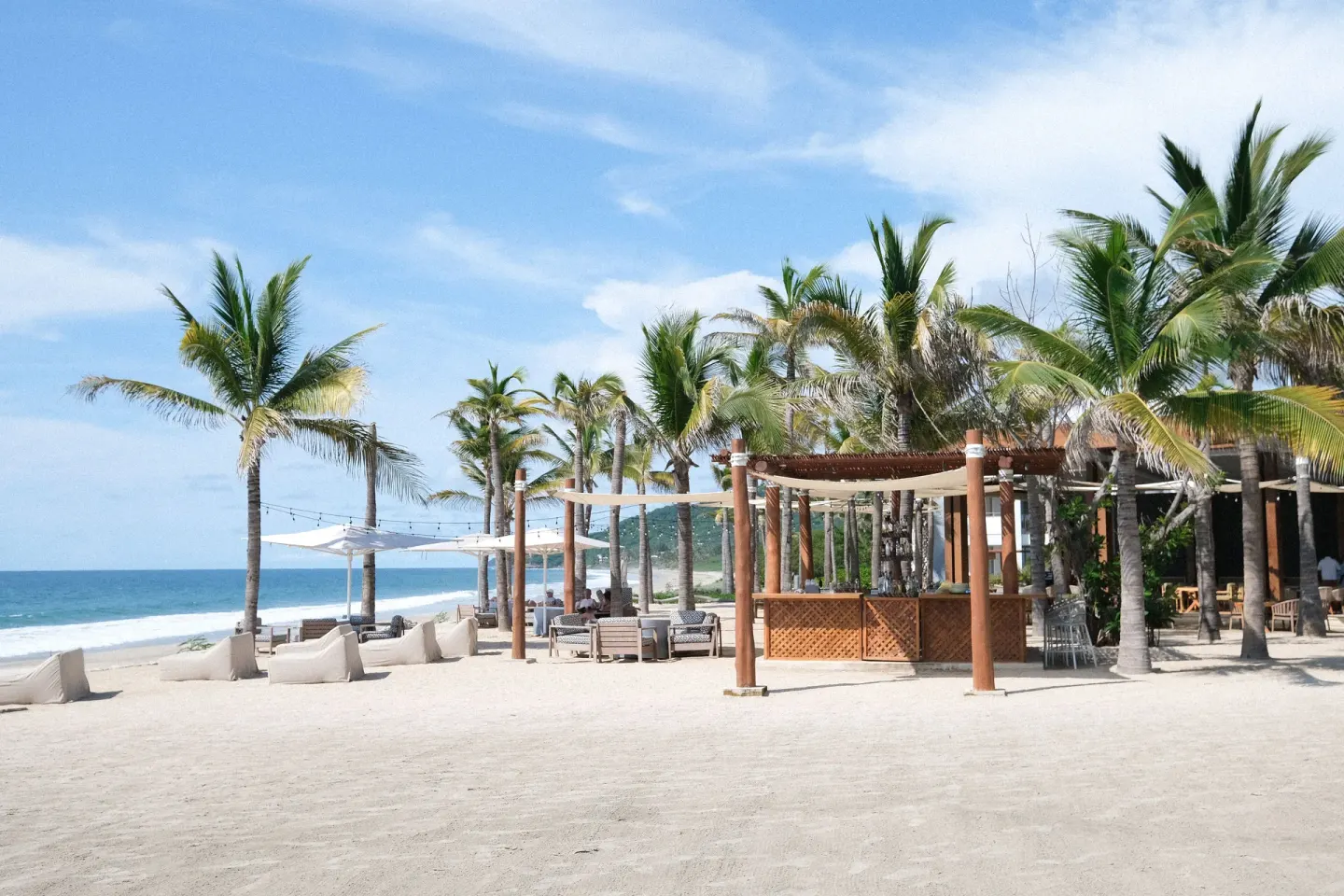 Beach lounge area with palms, shade canopies, and ocean at Conrad Punta de Mita.
