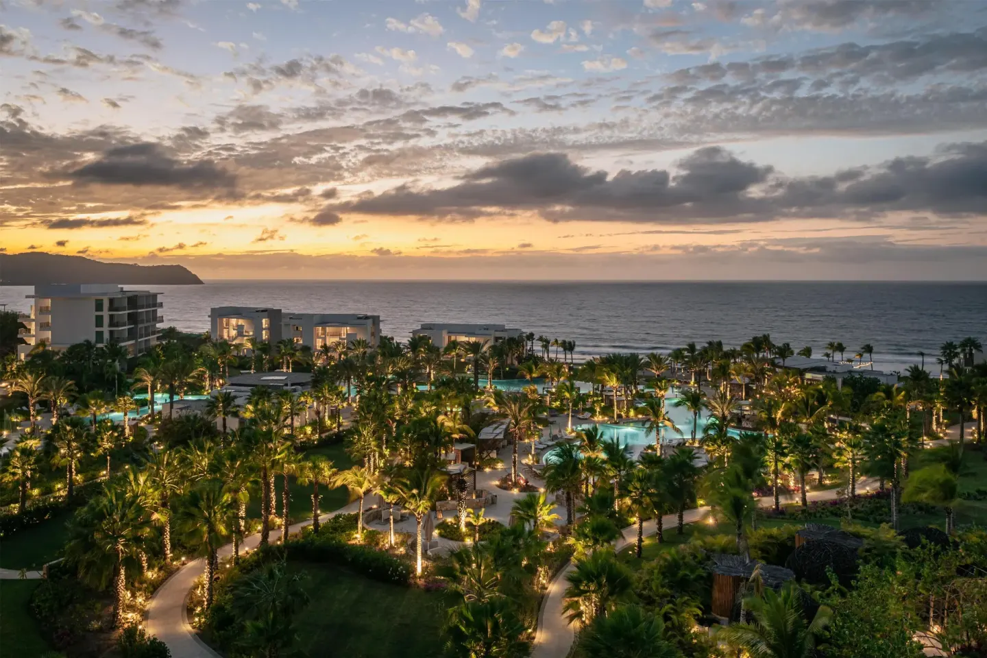 Illuminated resort grounds, pools, palms, and ocean at dusk at Conrad Punta de Mita.
