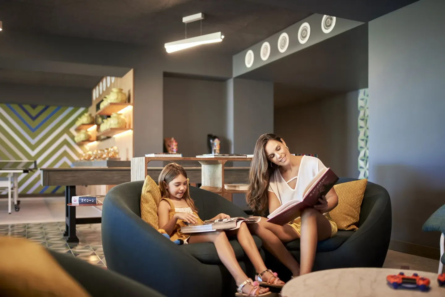 Adult and child reading on a curved sofa in a family lounge at Conrad Punta de Mita.