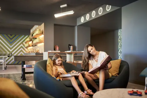 Adult and child reading on a curved sofa in a family lounge at Conrad Punta de Mita.