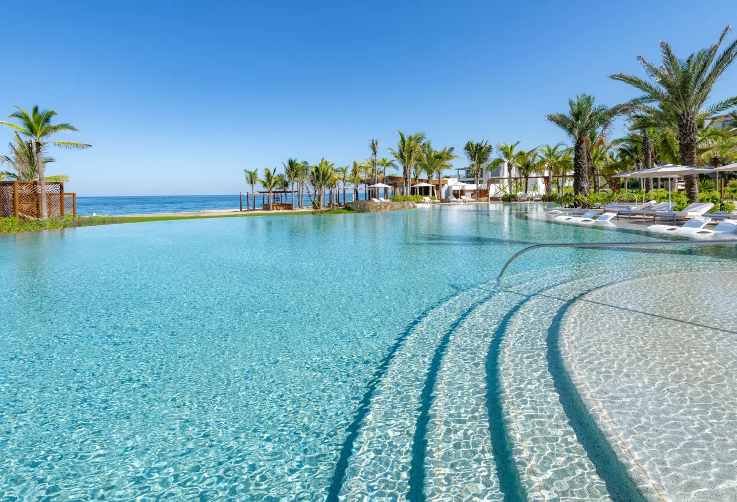 Wide infinity-style pool with steps, palms and ocean beyond at Conrad Punta de Mita.
