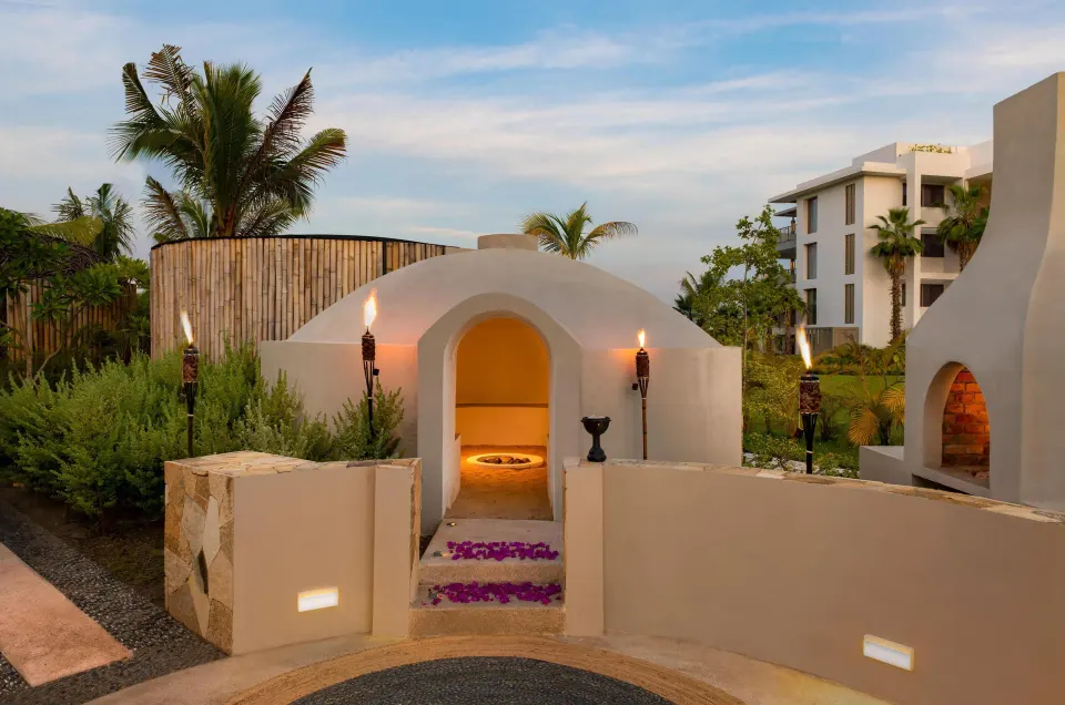 Outdoor temazcal-style spa structure with torches and gardens at Conrad Punta de Mita.