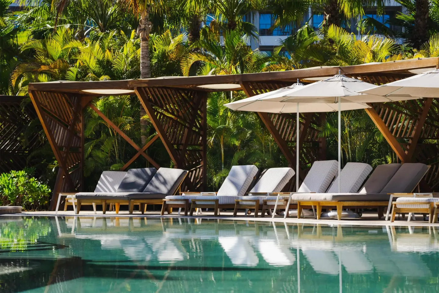 Poolside loungers and white umbrellas under palm trees at Conrad Punta de Mita.