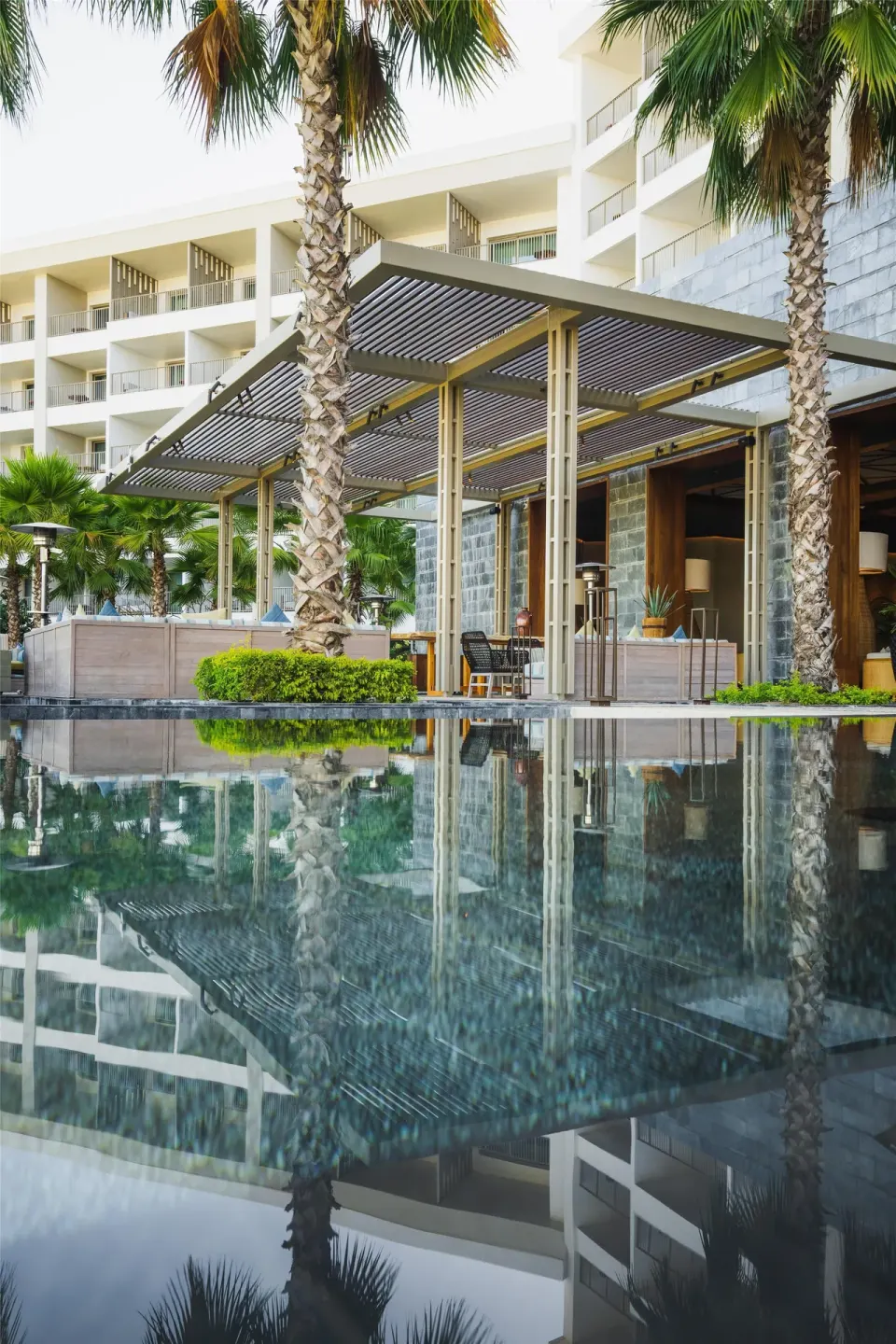 Poolside terrace with palms, pergola seating, and building reflections at Conrad Punta de Mita.