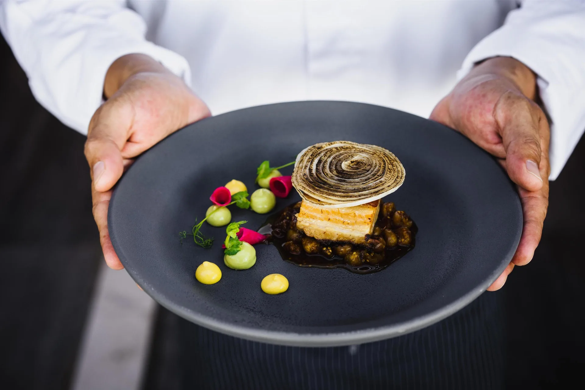 Chef holding a black plate with an artfully plated seafood dish at Conrad Punta de Mita.