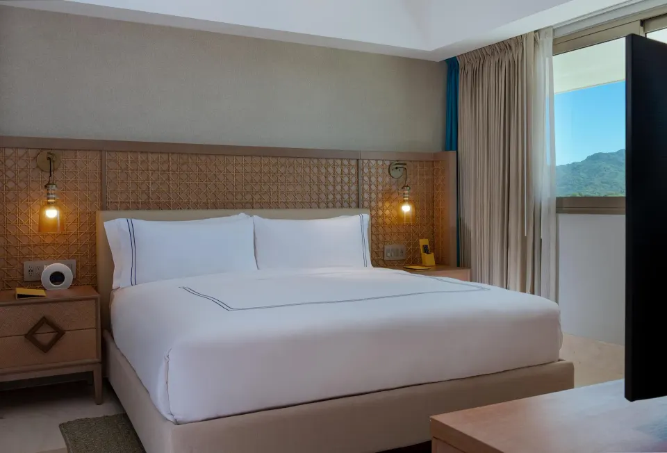 King bed and window in a two-bedroom ocean-view suite at Conrad Punta de Mita with woven headboard detail.