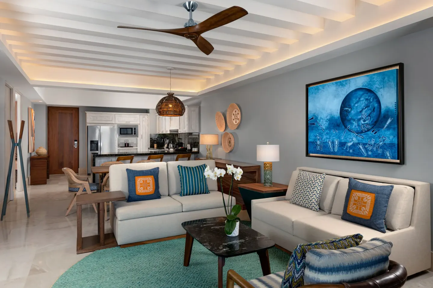 Two-bedroom suite living room and kitchen at Conrad Punta de Mita with sofas, dining area and blue wall art.