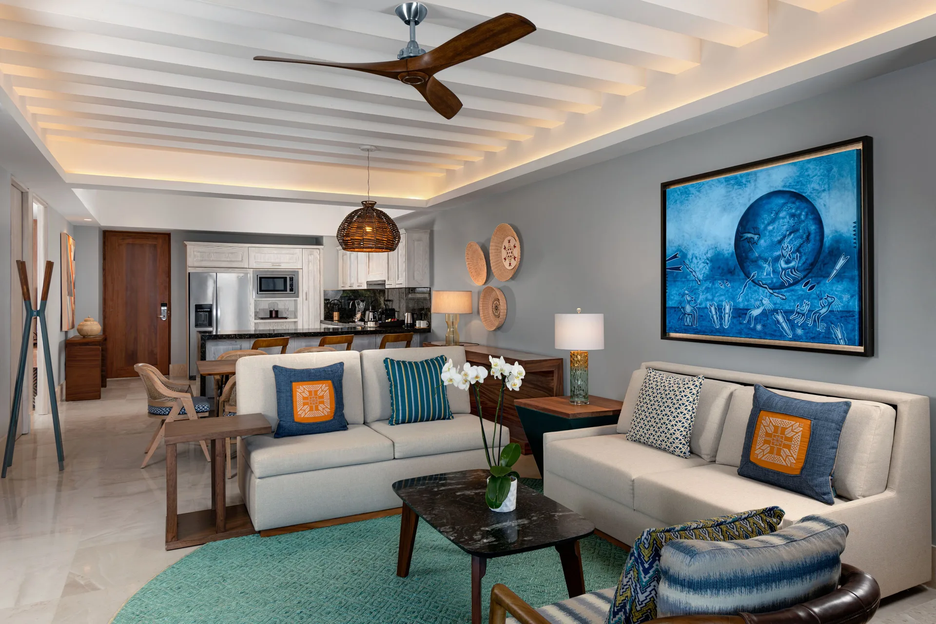 Two-bedroom suite living room and kitchen at Conrad Punta de Mita with sofas, dining area and blue wall art.