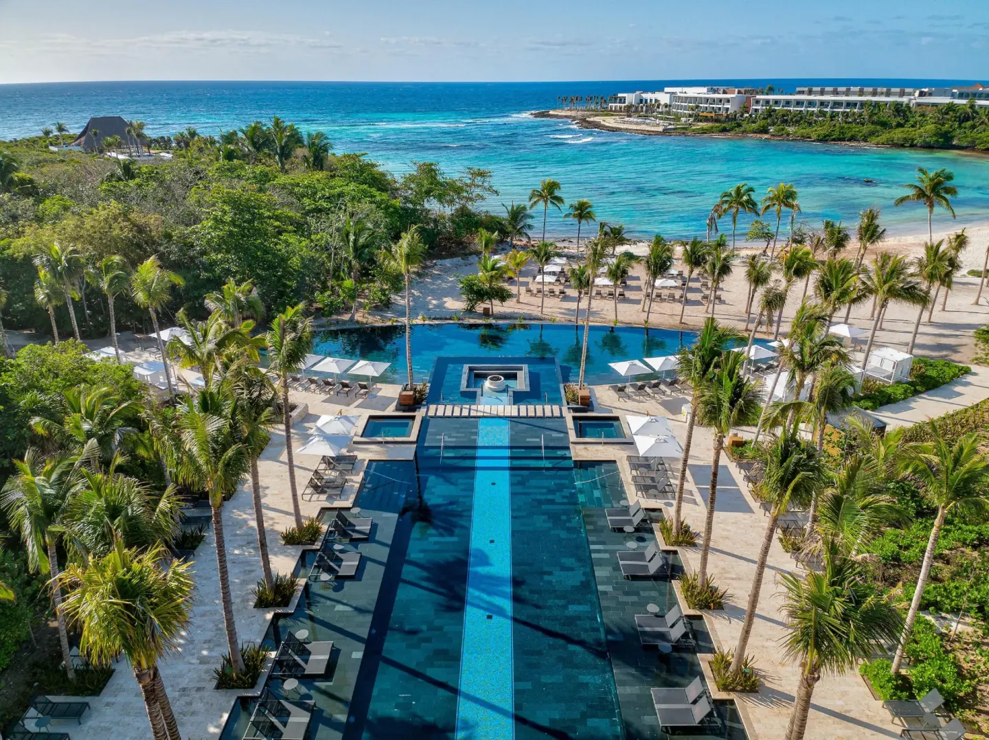 Aerial view of the pool and beach at Conrad Tulum Riviera Maya with palms, loungers, and turquoise sea.