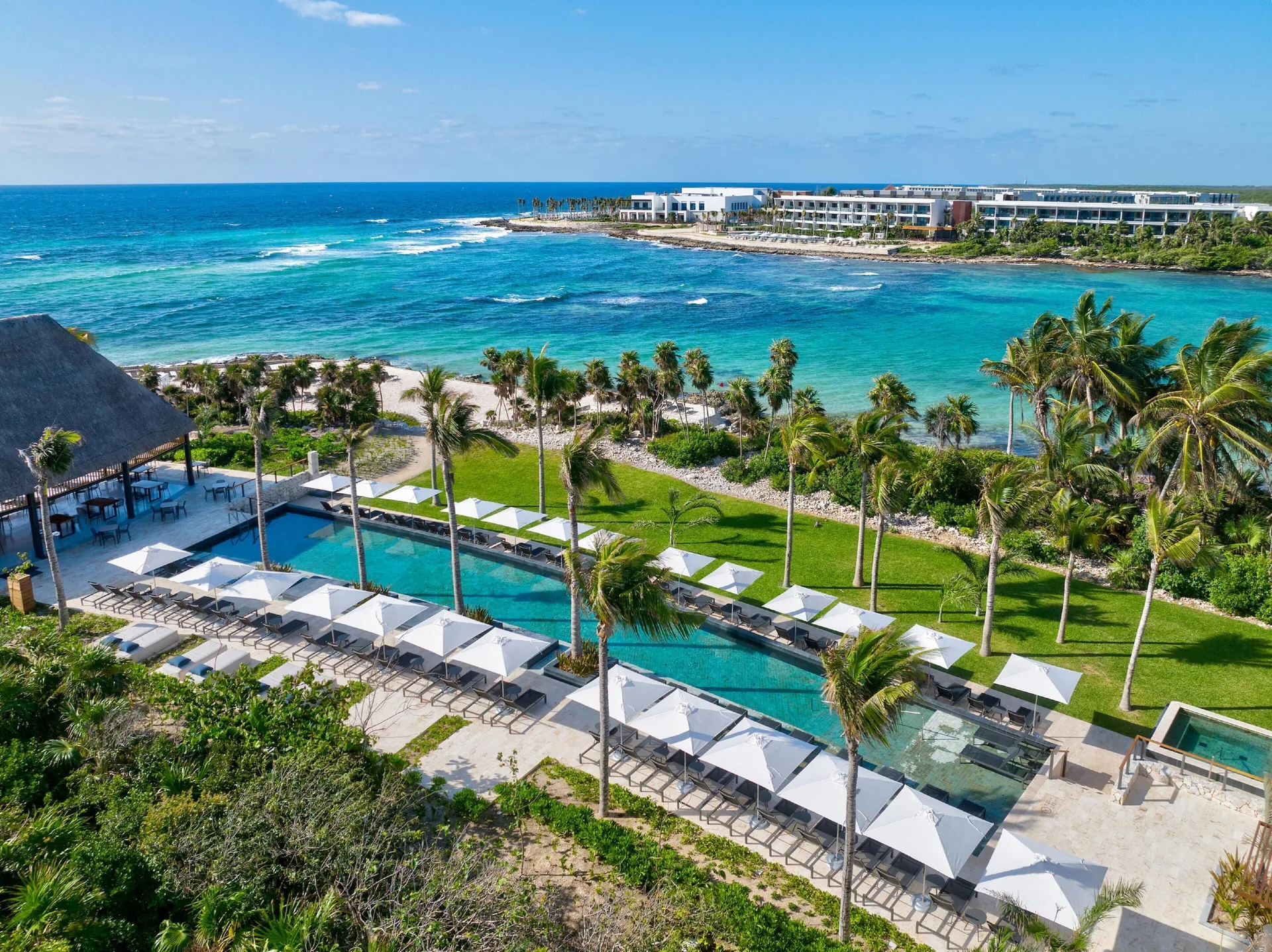 Elevated view of pools, palms, umbrellas and the Caribbean shoreline at Conrad Tulum Riviera Maya.