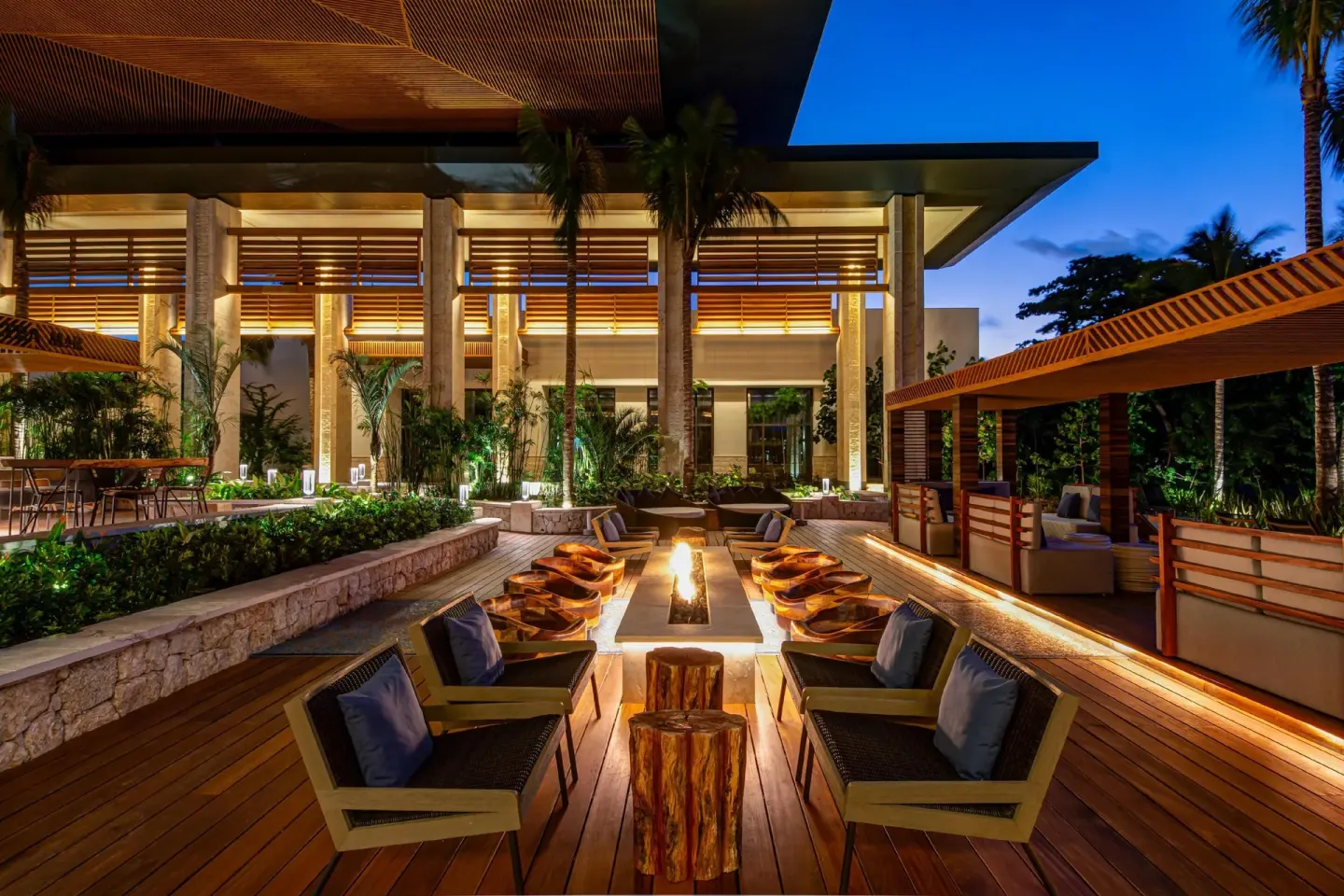 Fire pit lounge terrace at Conrad Tulum Riviera Maya with chairs, palms, and warm evening lighting.