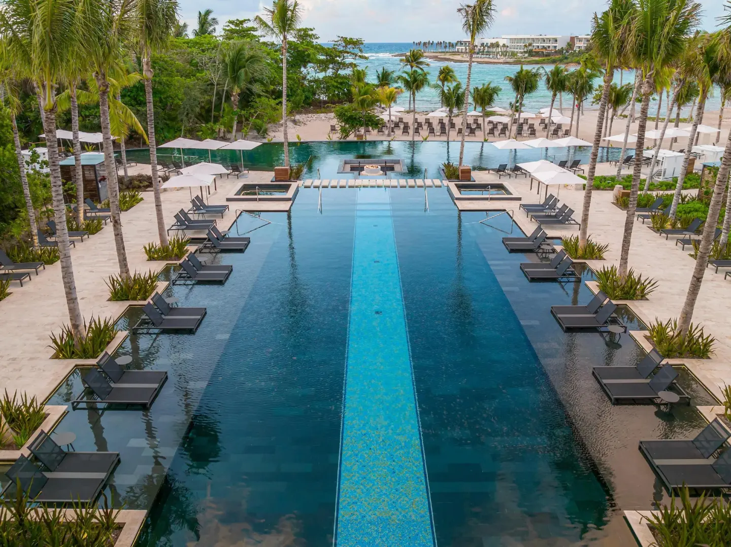 Infinity pool at Conrad Tulum Riviera Maya with in-water loungers, palms, umbrellas, and the beach beyond.
