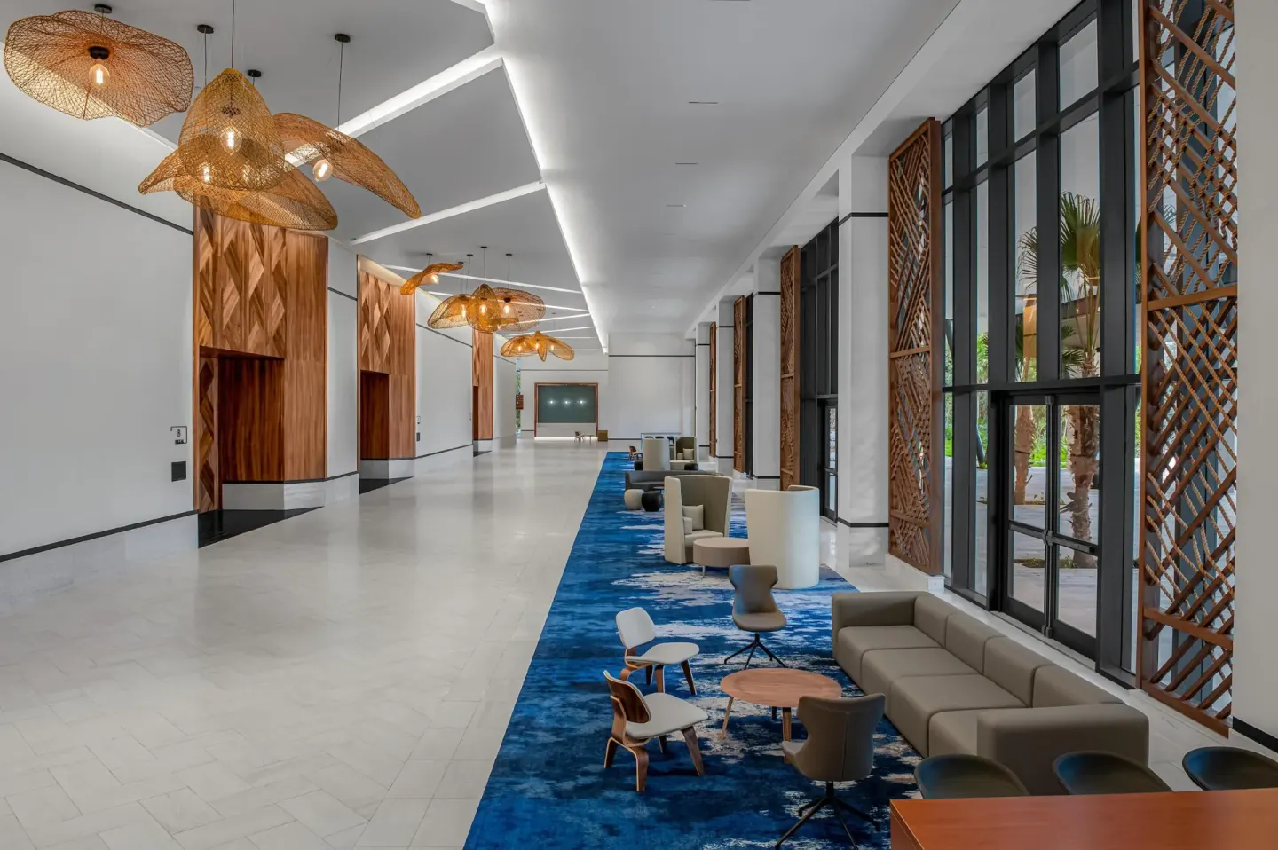 Long lobby lounge with tall windows and blue carpet at Conrad Tulum Riviera Maya.