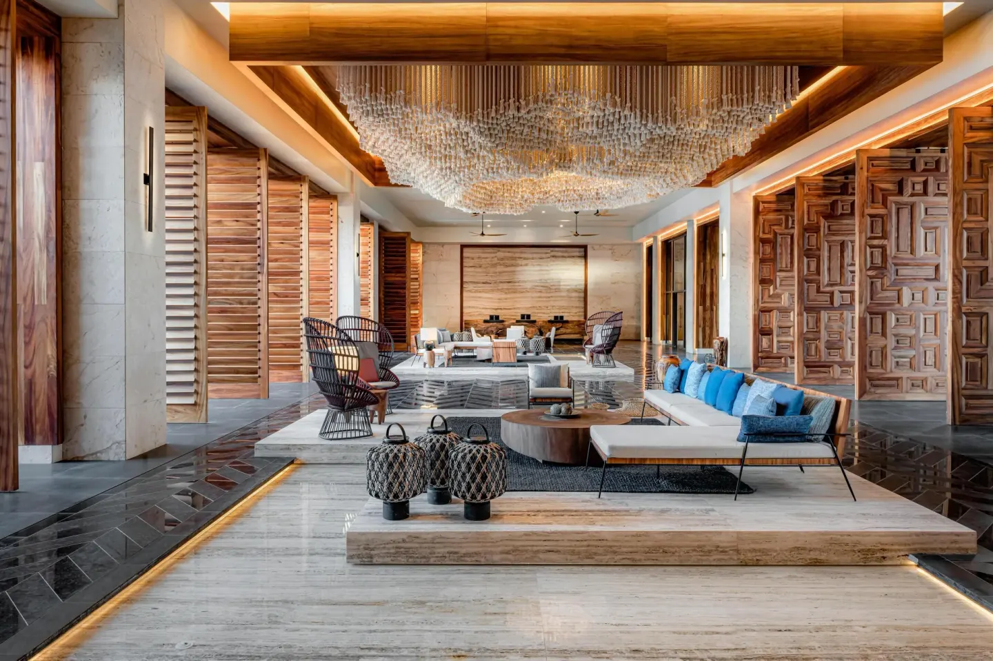 Lobby seating with blue pillows, wood panels, and chandelier at Conrad Tulum Riviera Maya.