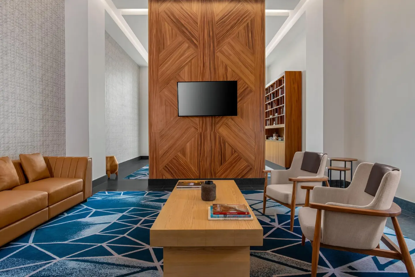Modern lounge with leather sofa, armchairs, wood wall, and TV at Conrad Tulum Riviera Maya.