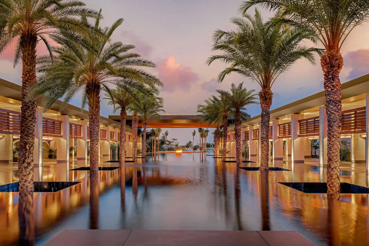 Palm-lined reflecting pools at Conrad Tulum Riviera Maya at sunset with warm architectural lighting.