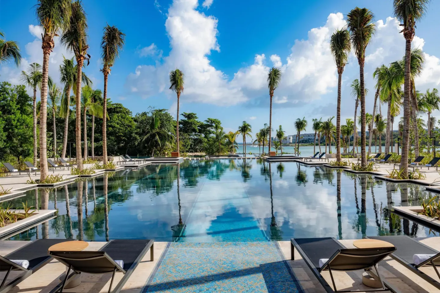 Pool with loungers, palm trees, and ocean in the distance at Conrad Tulum Riviera Maya.