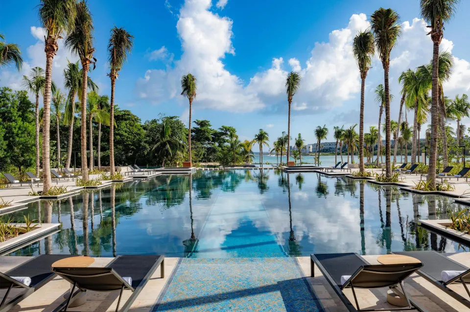 Pool with loungers, palm trees, and ocean in the distance at Conrad Tulum Riviera Maya.