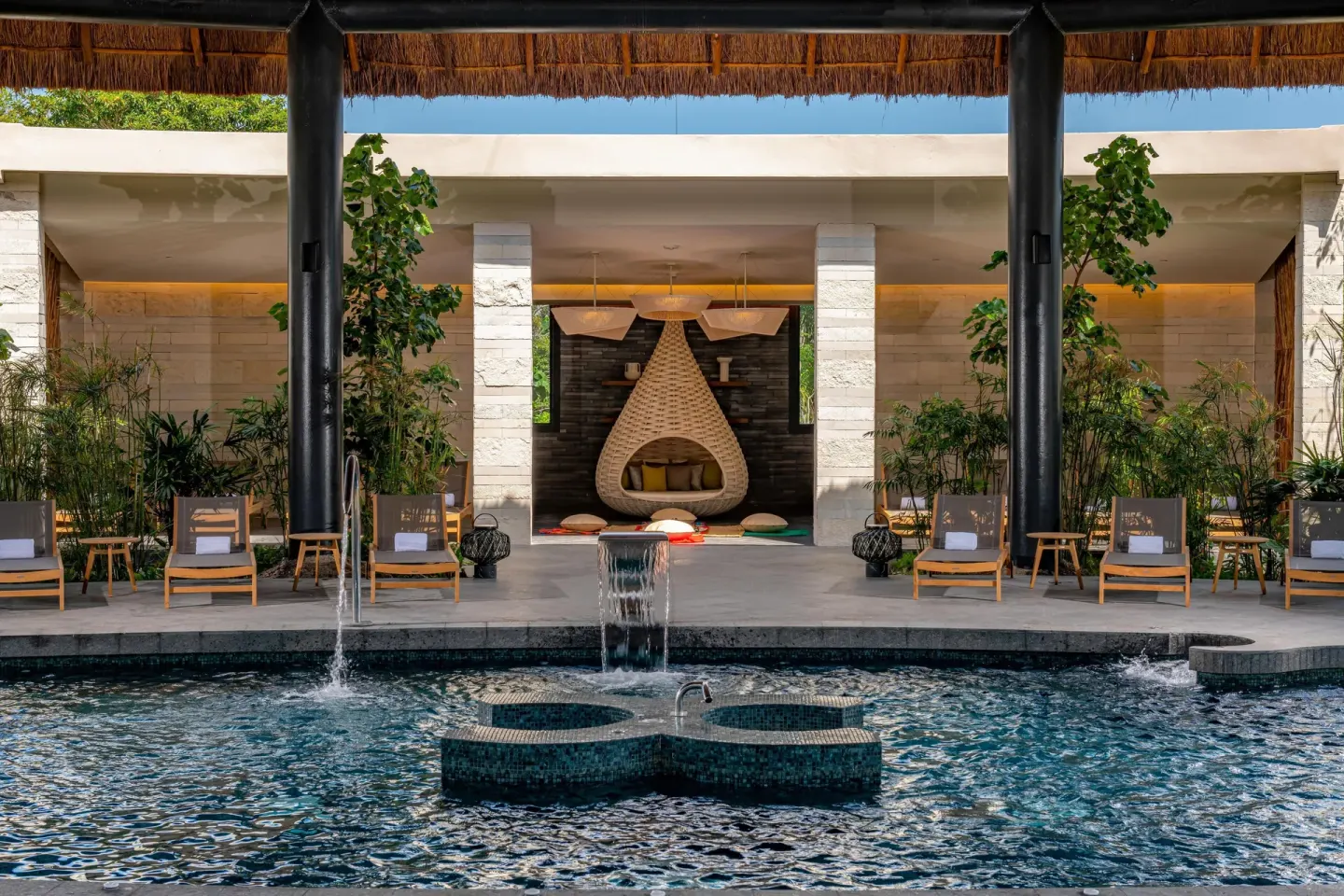 Pool with fountains, loungers, and a hanging nest seat at Conrad Tulum Riviera Maya.