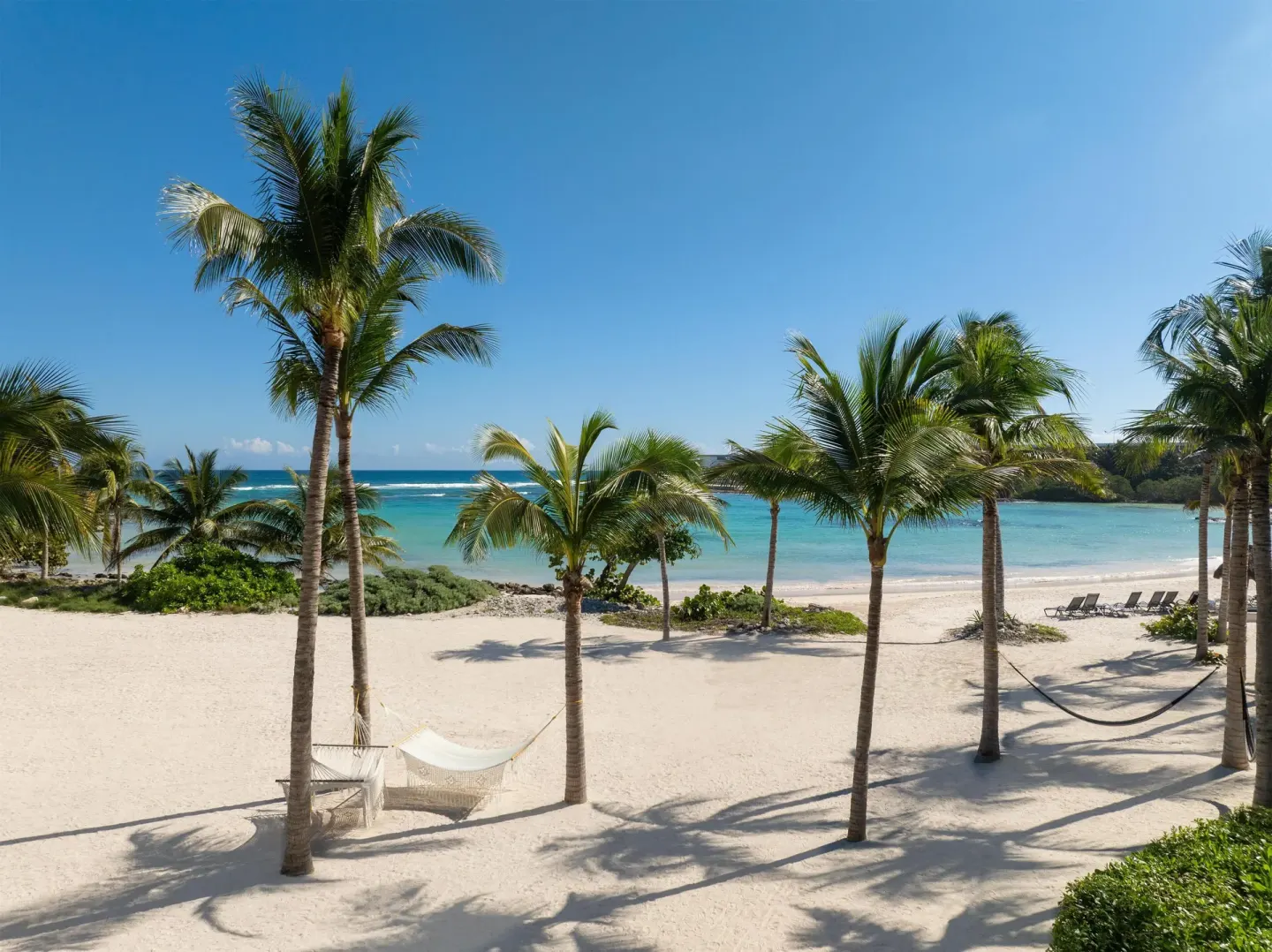 White sand beach at Conrad Tulum Riviera Maya with palm trees, hammocks, lounge chairs, and turquoise water.