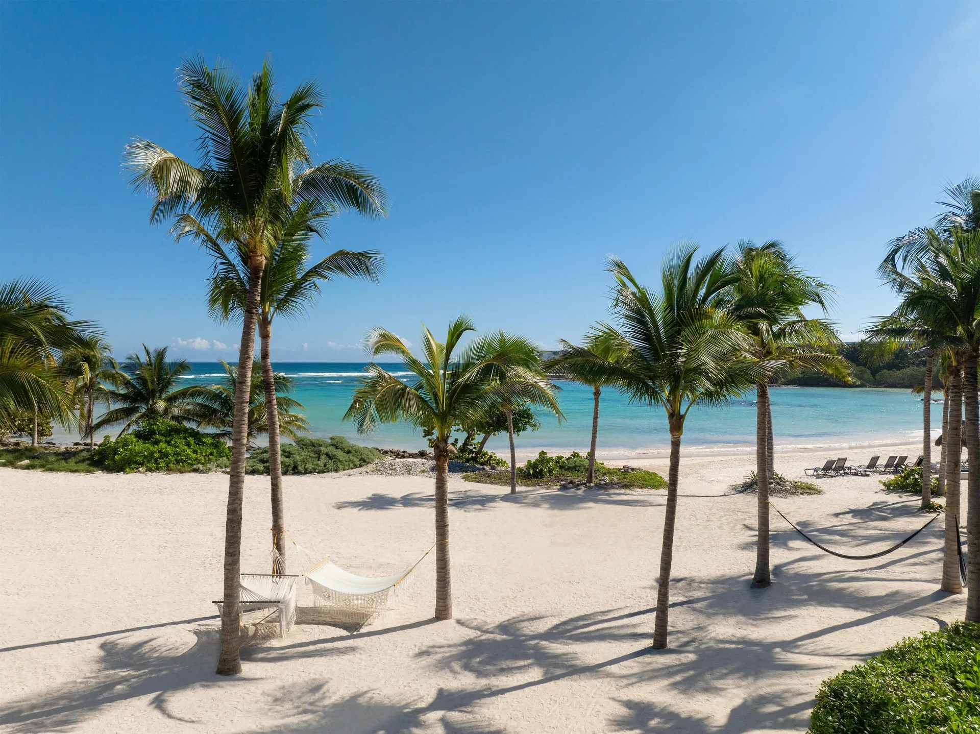 White sand beach at Conrad Tulum Riviera Maya with palm trees, hammocks, lounge chairs, and turquoise water.