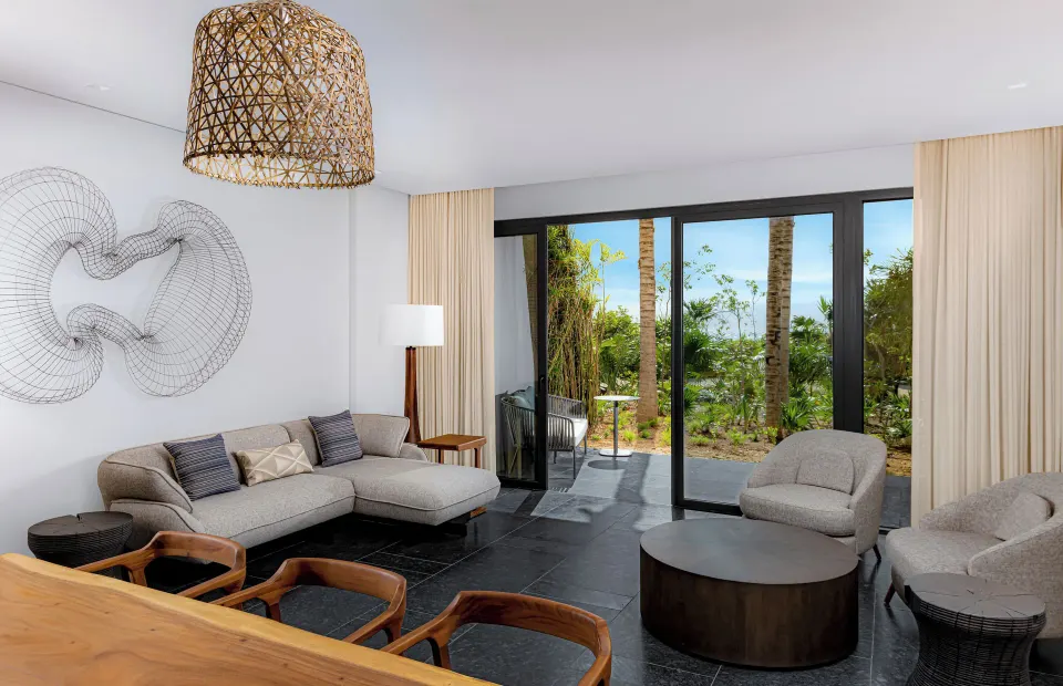Tropical View Guestroom living area at Conrad Tulum Riviera Maya with sofa and garden-facing glass doors.