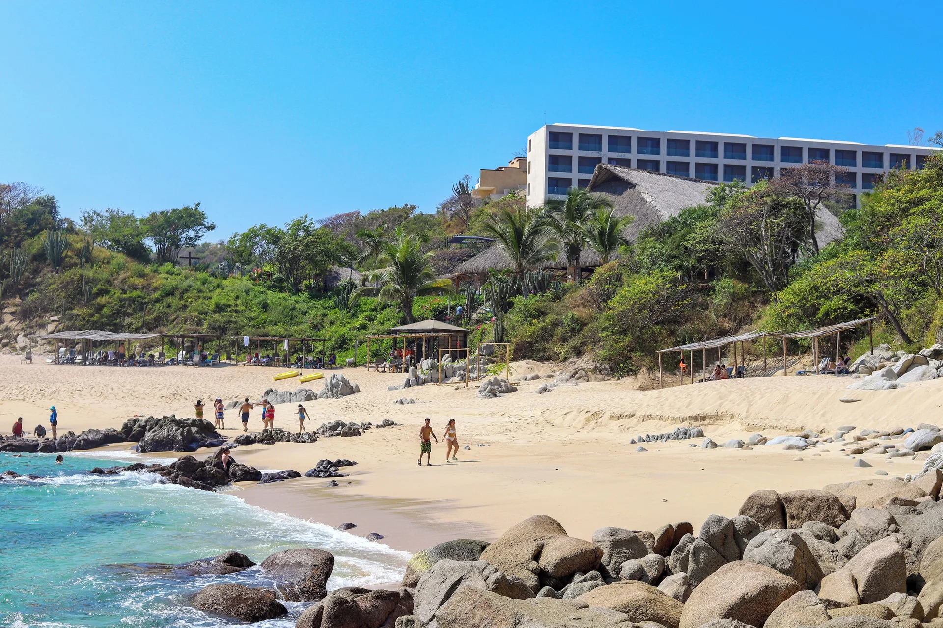 Beach cove with rocks, swimmers, and the resort building at Coral Blue Huatulco.