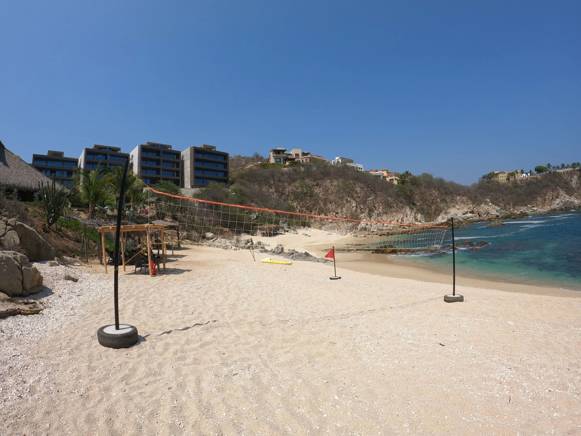 Wide beach volleyball setup with resort buildings on the hillside at Coral Blue Huatulco.