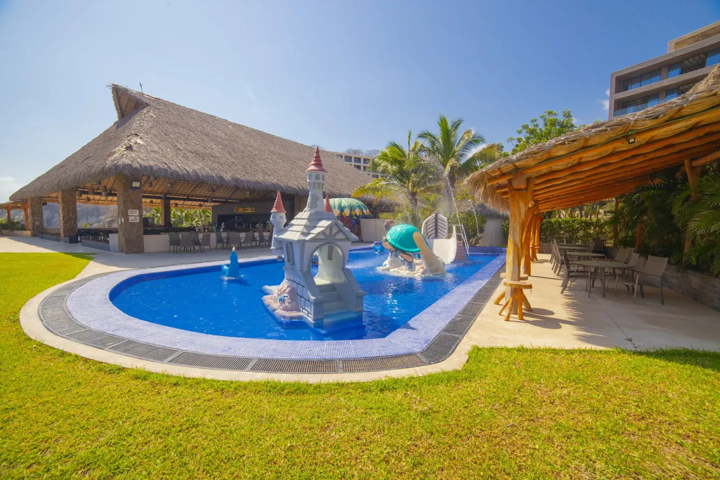 Children's splash pool with castle slide and palapa seating at Coral Blue Huatulco.