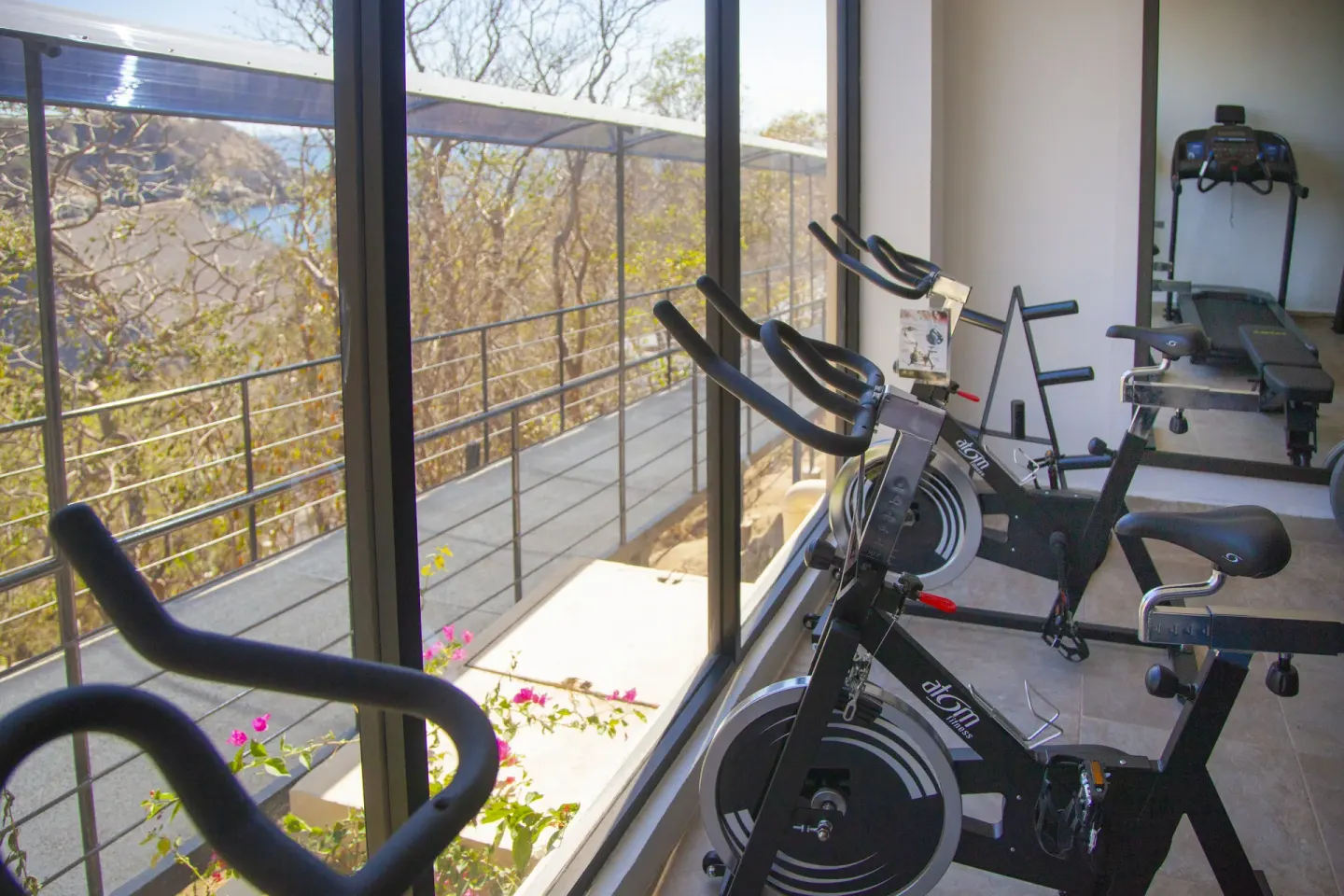 Fitness room bikes beside tall windows with a coastal view at Coral Blue Huatulco.
