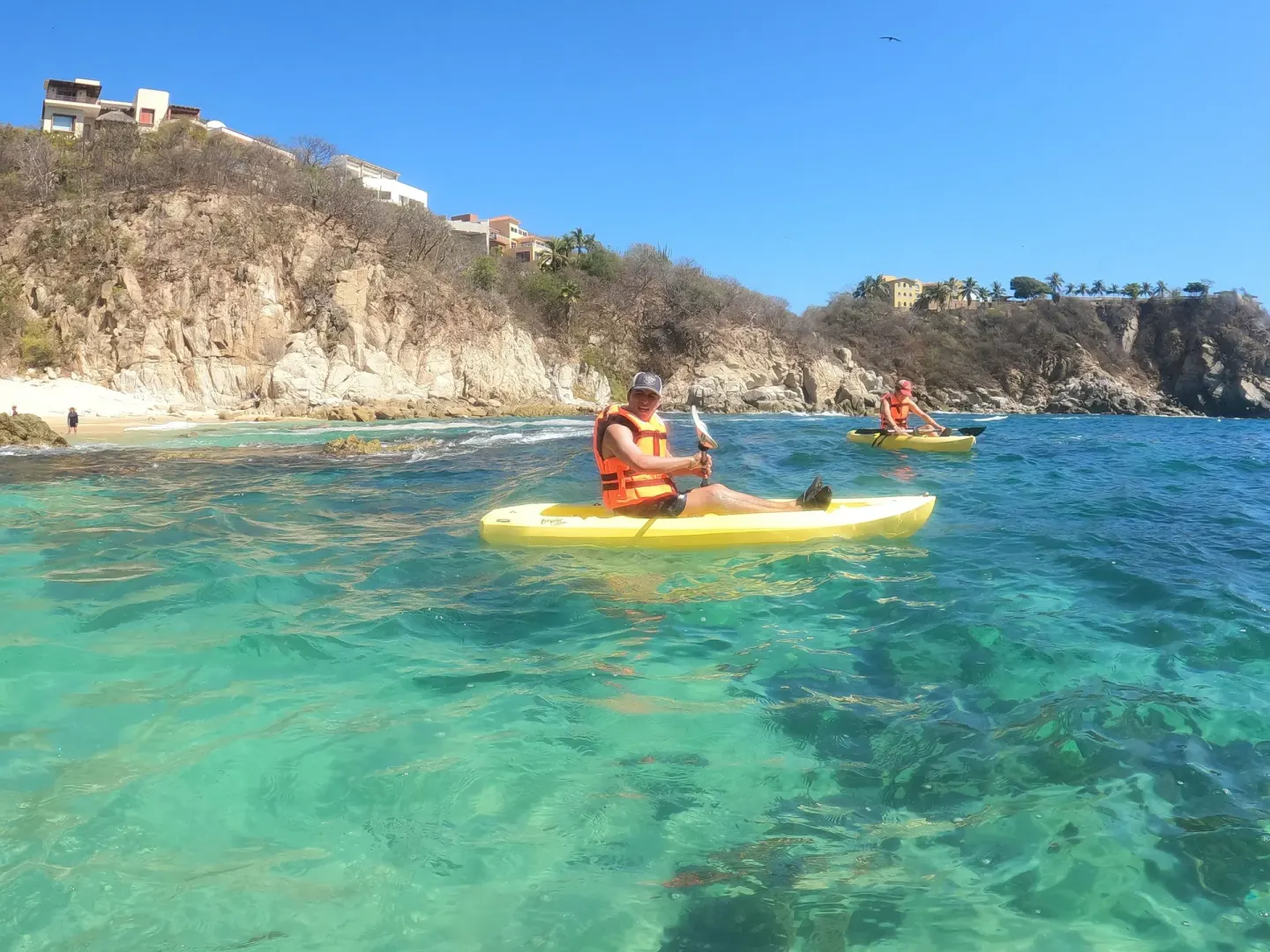 Kayakers in clear blue water near rocky cliffs at Coral Blue Huatulco.