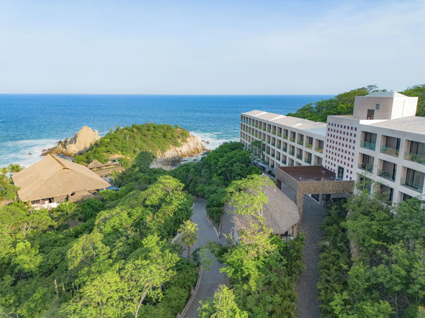 Coral Blue Huatulco guest room building beside trees, rocky coastline, and ocean.